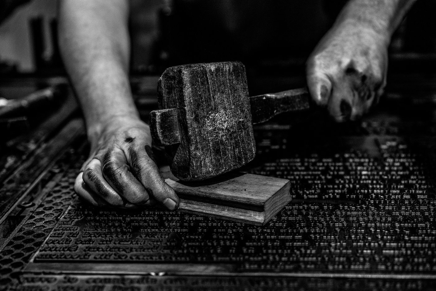 A compositor taps a planer with a hammer to straighten out type in a forme