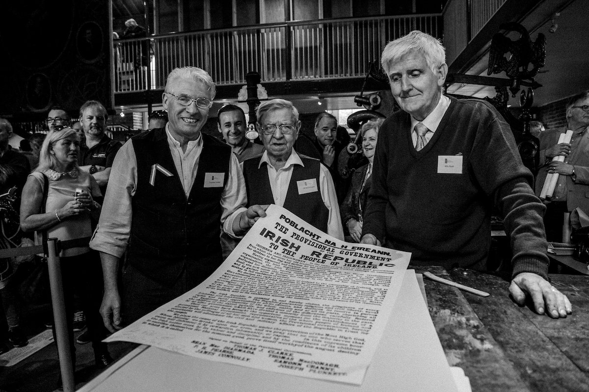 Three retired printers hold up a replica Proclamation