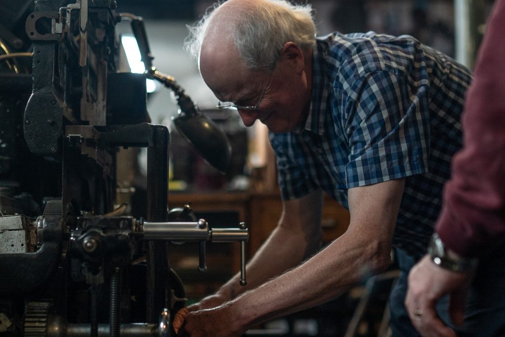 A retired compositor bends down to demonstrate the Linotype machine