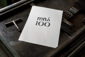 'Mna 100' printed in Gaelic type on paper and resting on a printing press bed