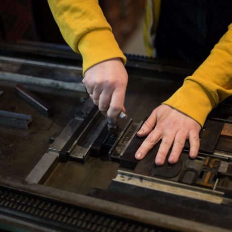 A letterpress printer tightens a forme using a quoin key.
