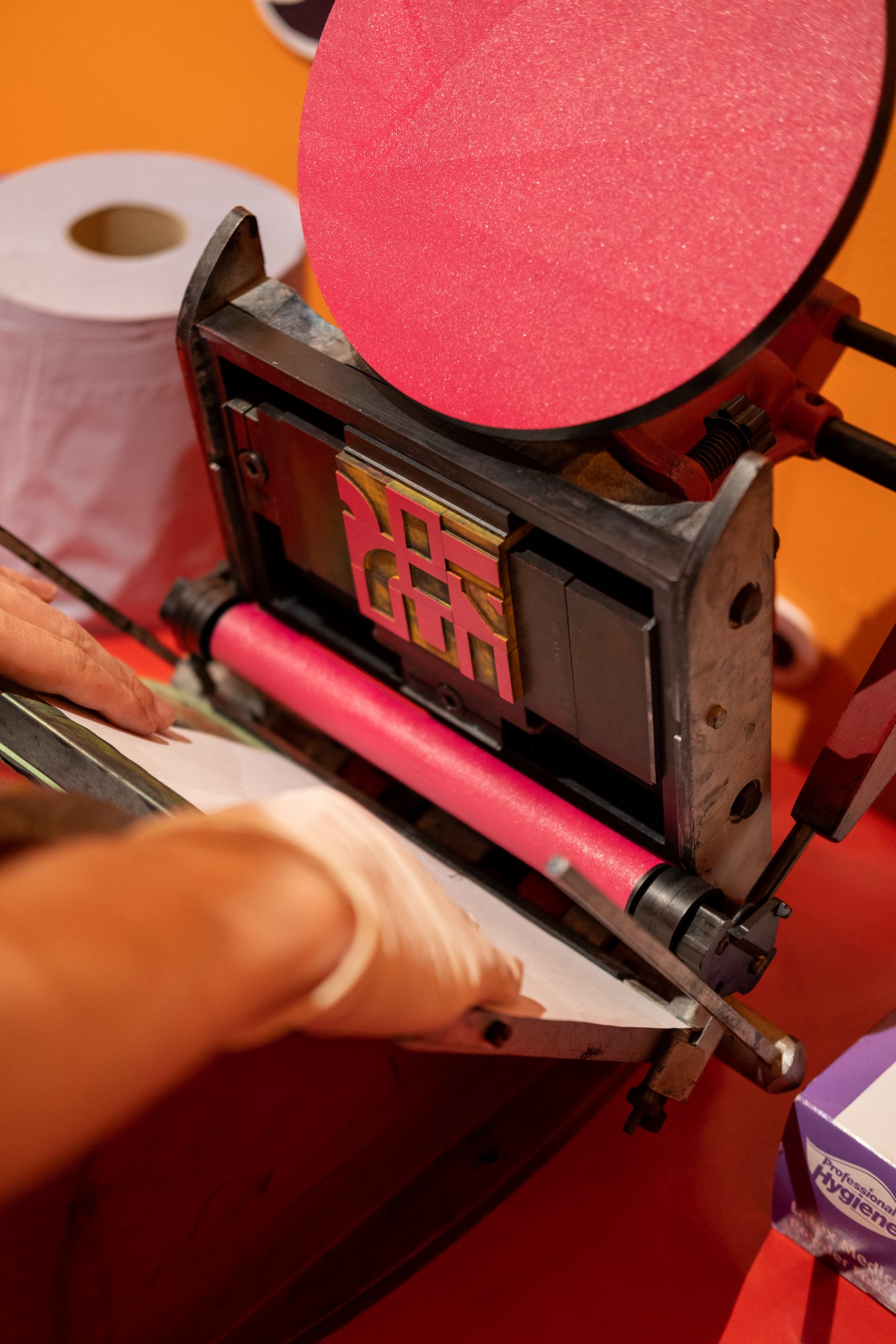 Paper is fed into a small Adana press, which is loaded with pink ink.
