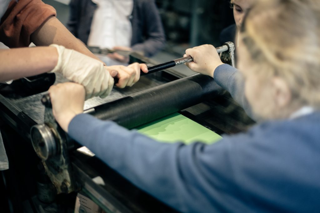 A child pulls a print on a proofing press during their tour.
