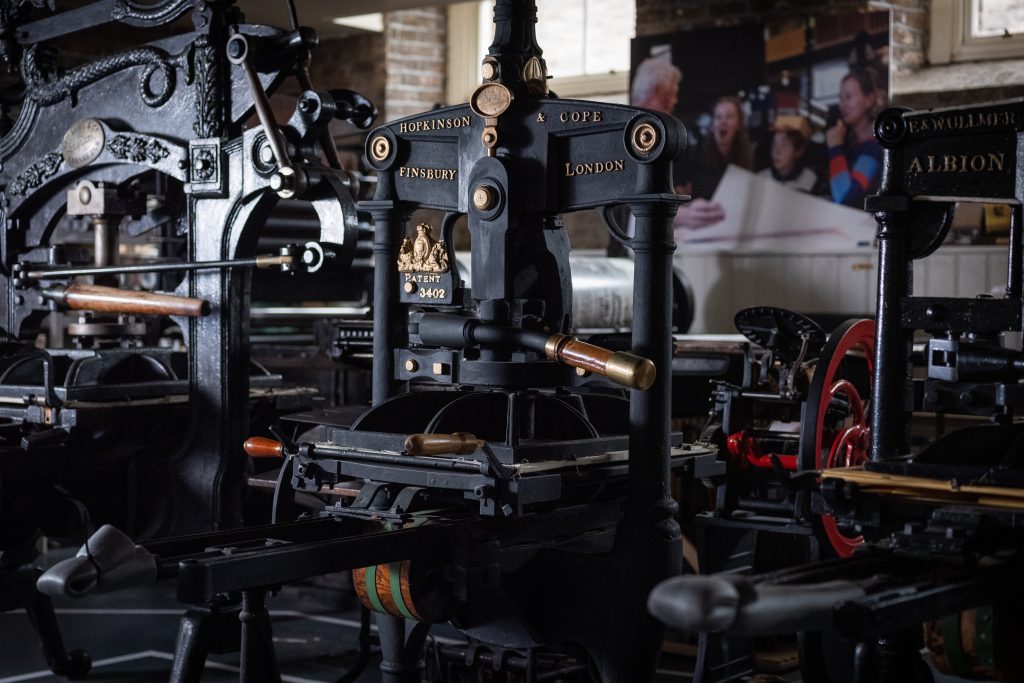 An image centered on the black Hopkinson & Cope printing press, flanked by Columbian and Albion presses