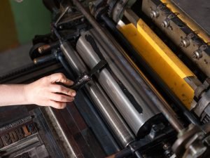 Using a spatula to apply ink to a roller on a Vandercook press.