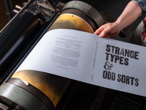 Pulling a freshly printed book dustjacket from a printing press.