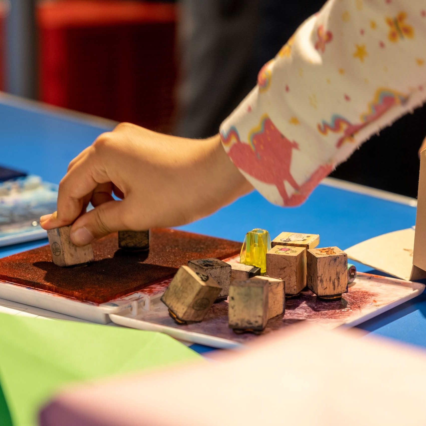 A child's hand pressing a stamp into a red ink pad.