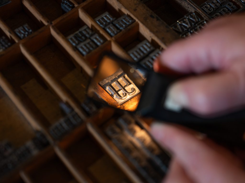 A magnifying glass is held up to metal type in a case