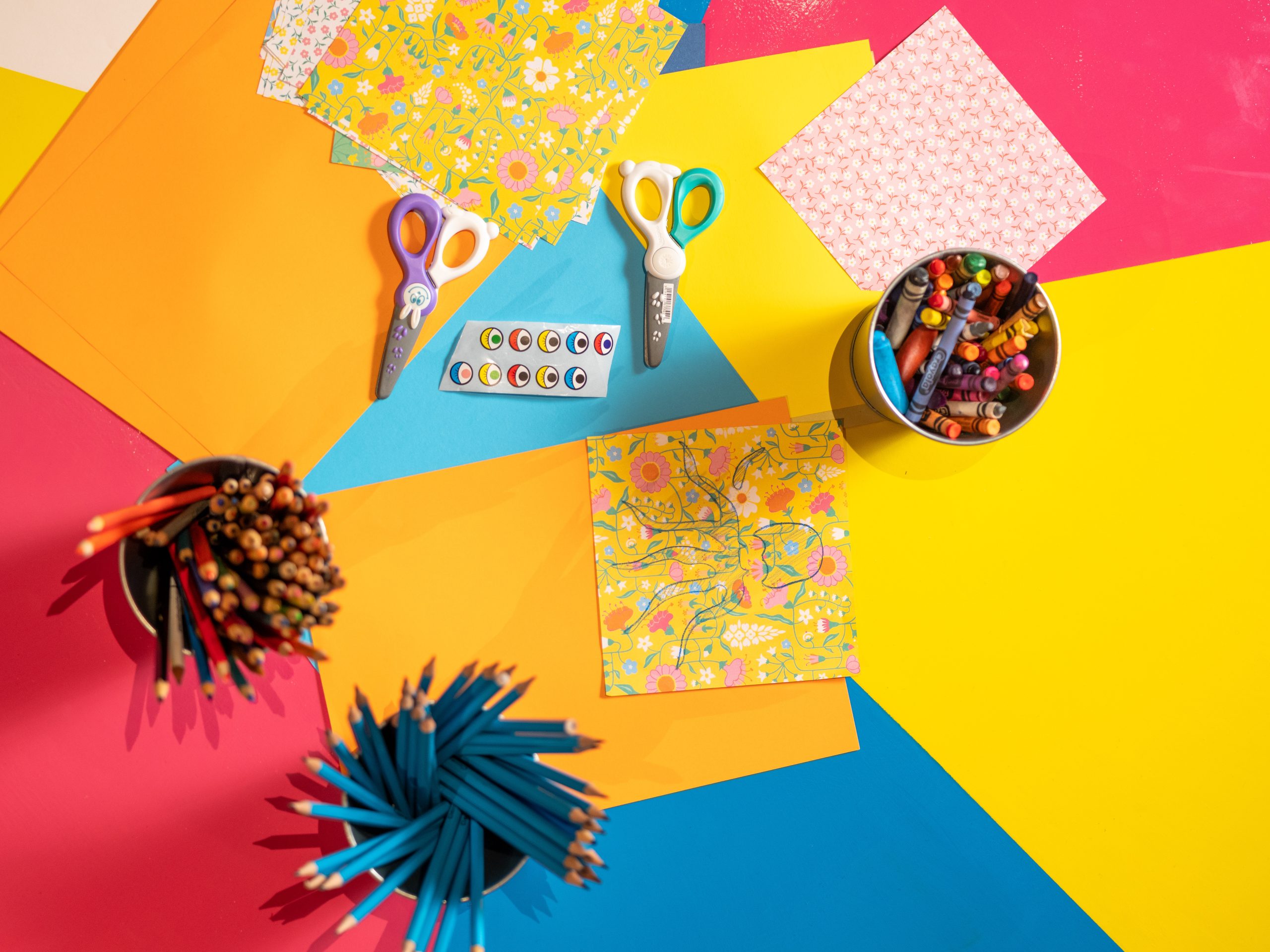 A photo of the tabletop in the Education Area, with containers of coloured pencils and crayons, patterned origami paper, scissors, and stickers