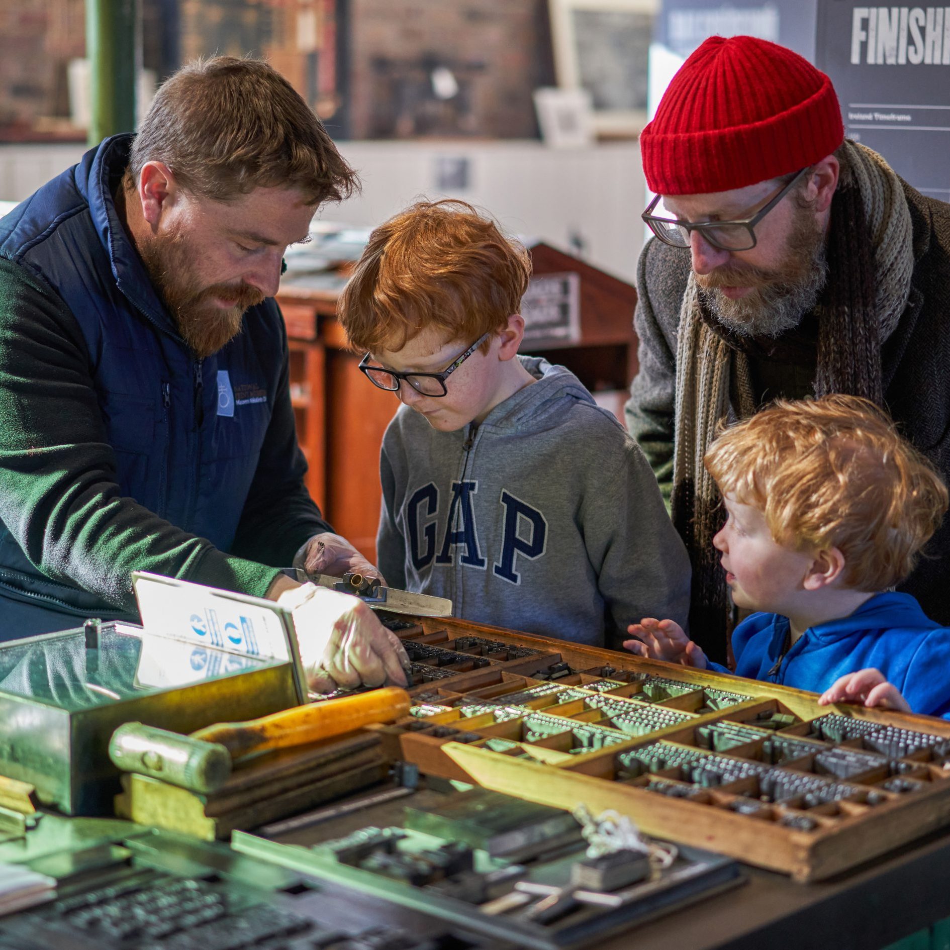 An adult and 2 children are shown a case of type by a tour guide during their visit to the Museum